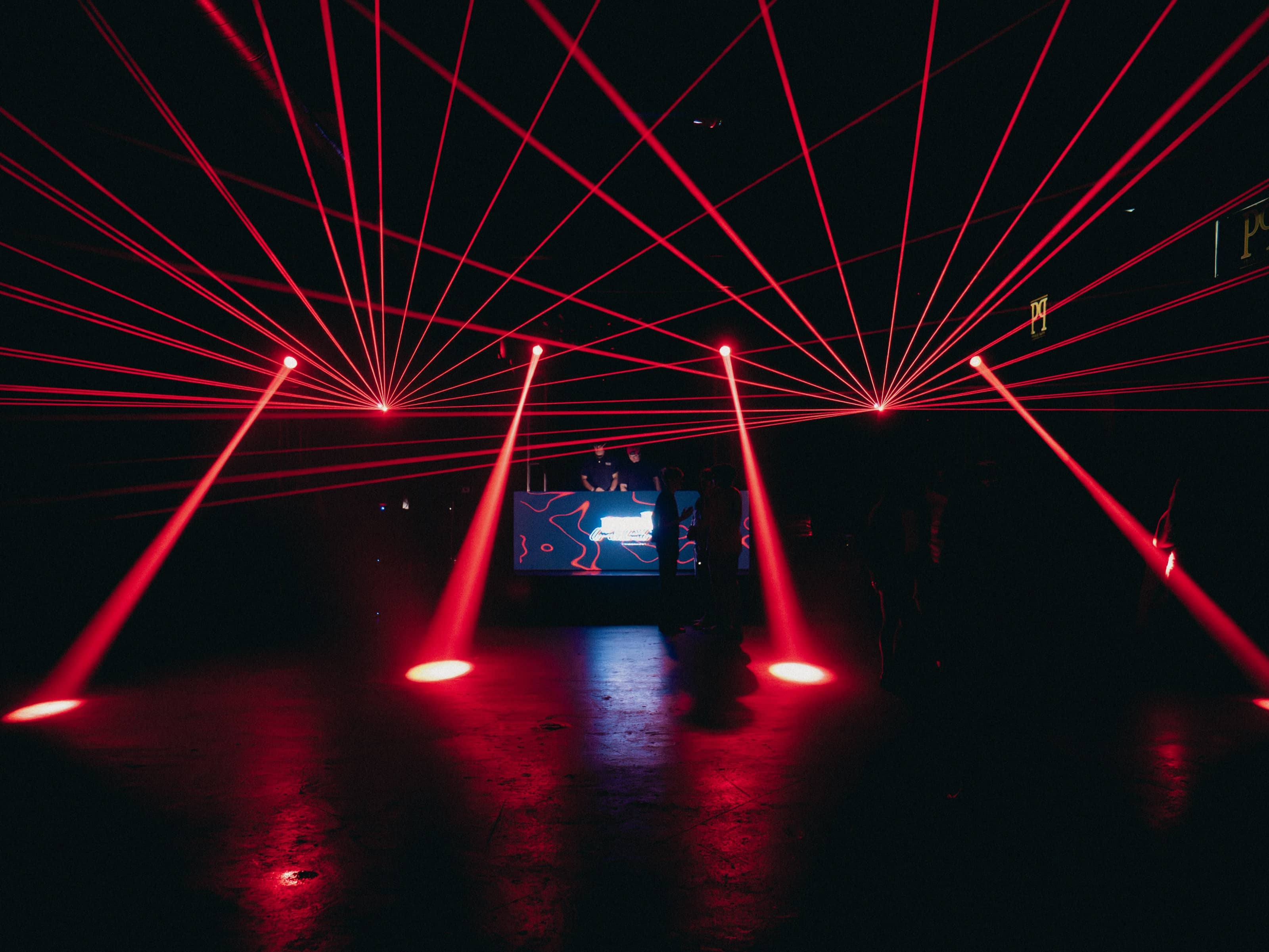 Red laser beams radiating across a dark venue over the DJ booth, pools of red light on the floor