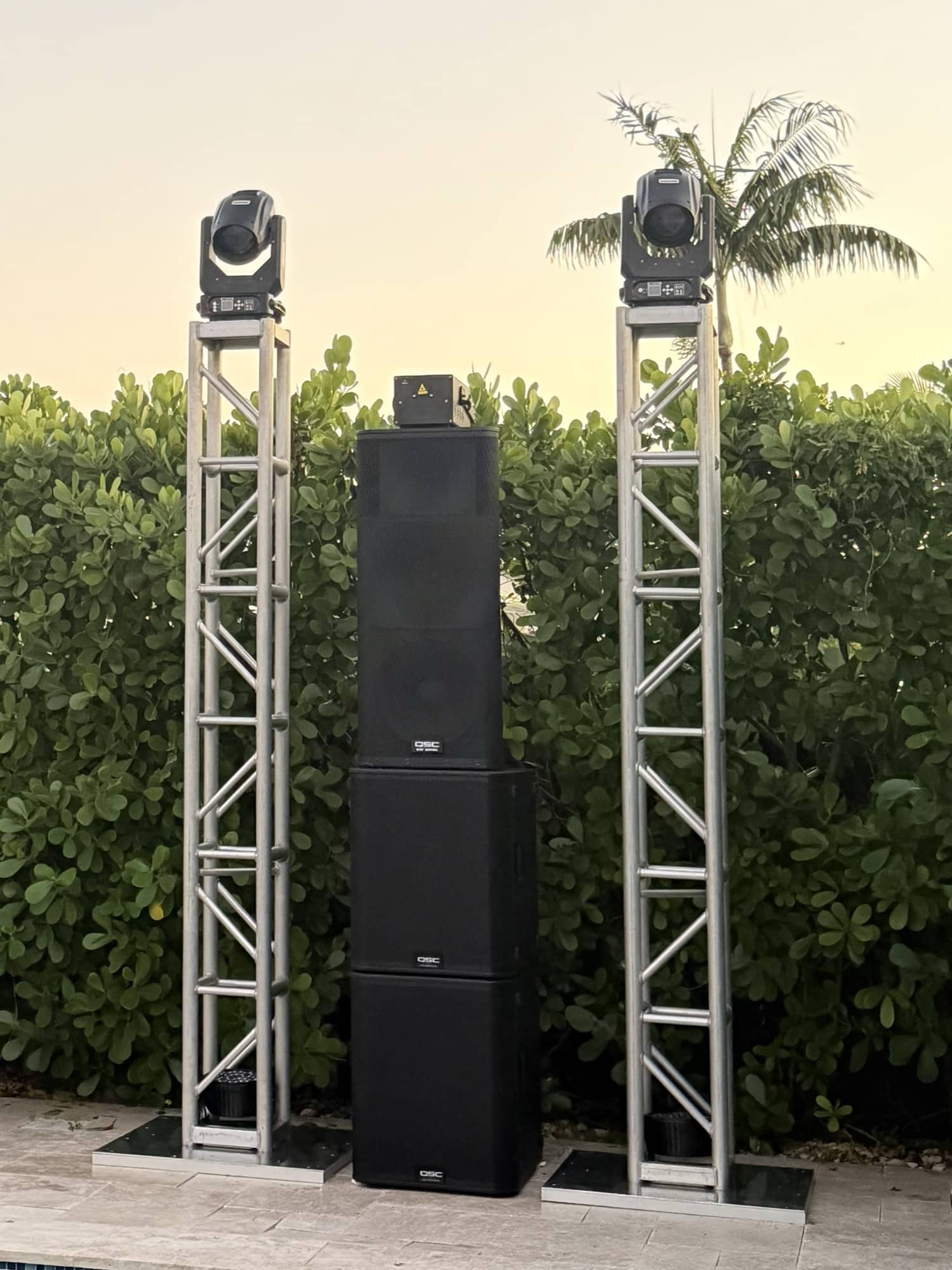Truss totems with moving heads and a PA stack beside a backyard pool at dusk