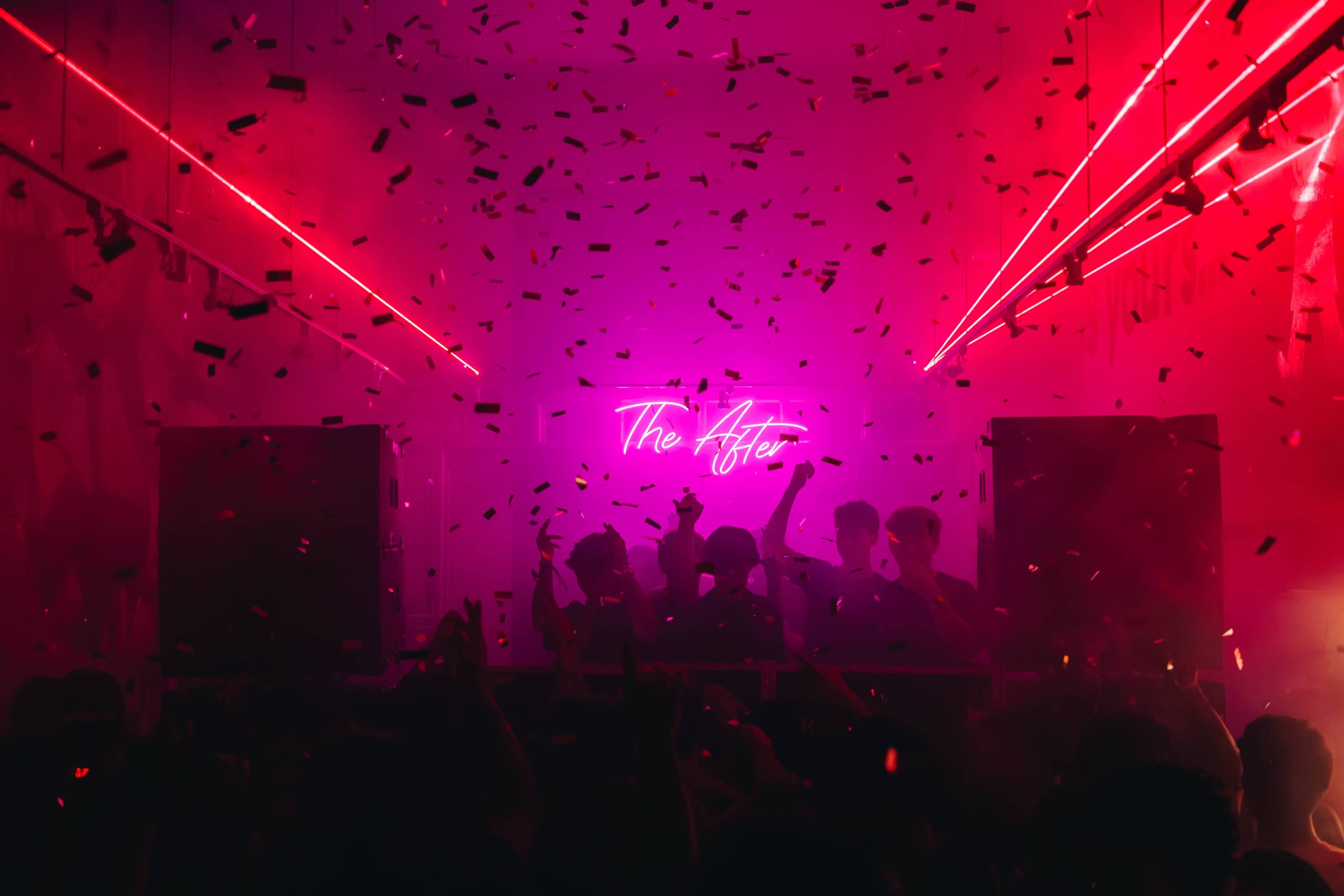 Confetti falling through red laser beams over a full dance floor, with The After neon sign glowing pink at the back of the room